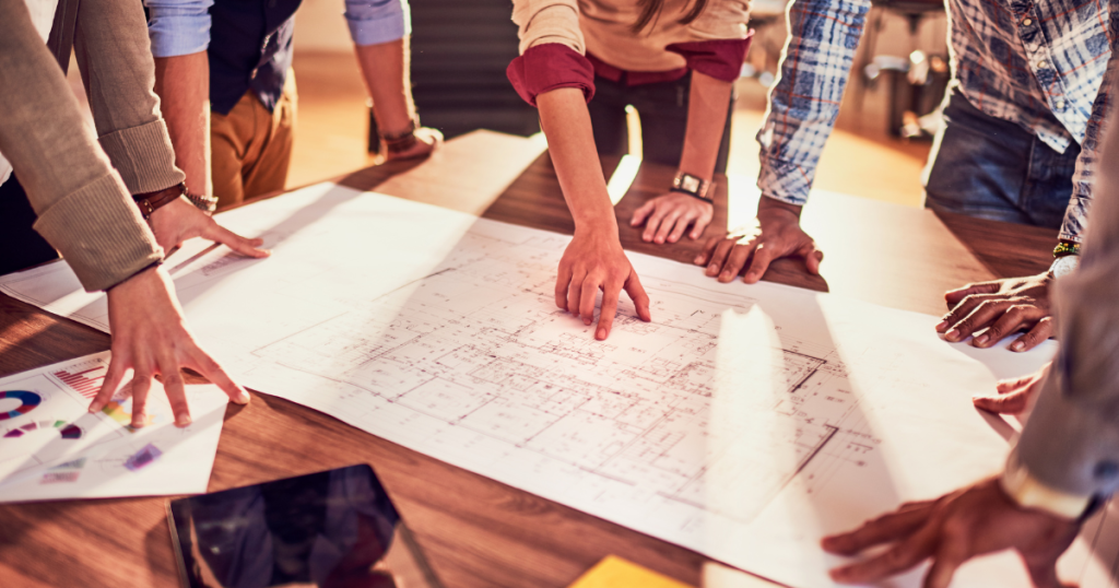Team of urban planners and architects reviewing building blueprints and charts during a collaborative planning meeting around a table